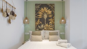 A neatly made bed with a floral-patterned bedspread, two bedside lamps, and a large botanical painting on the wall.