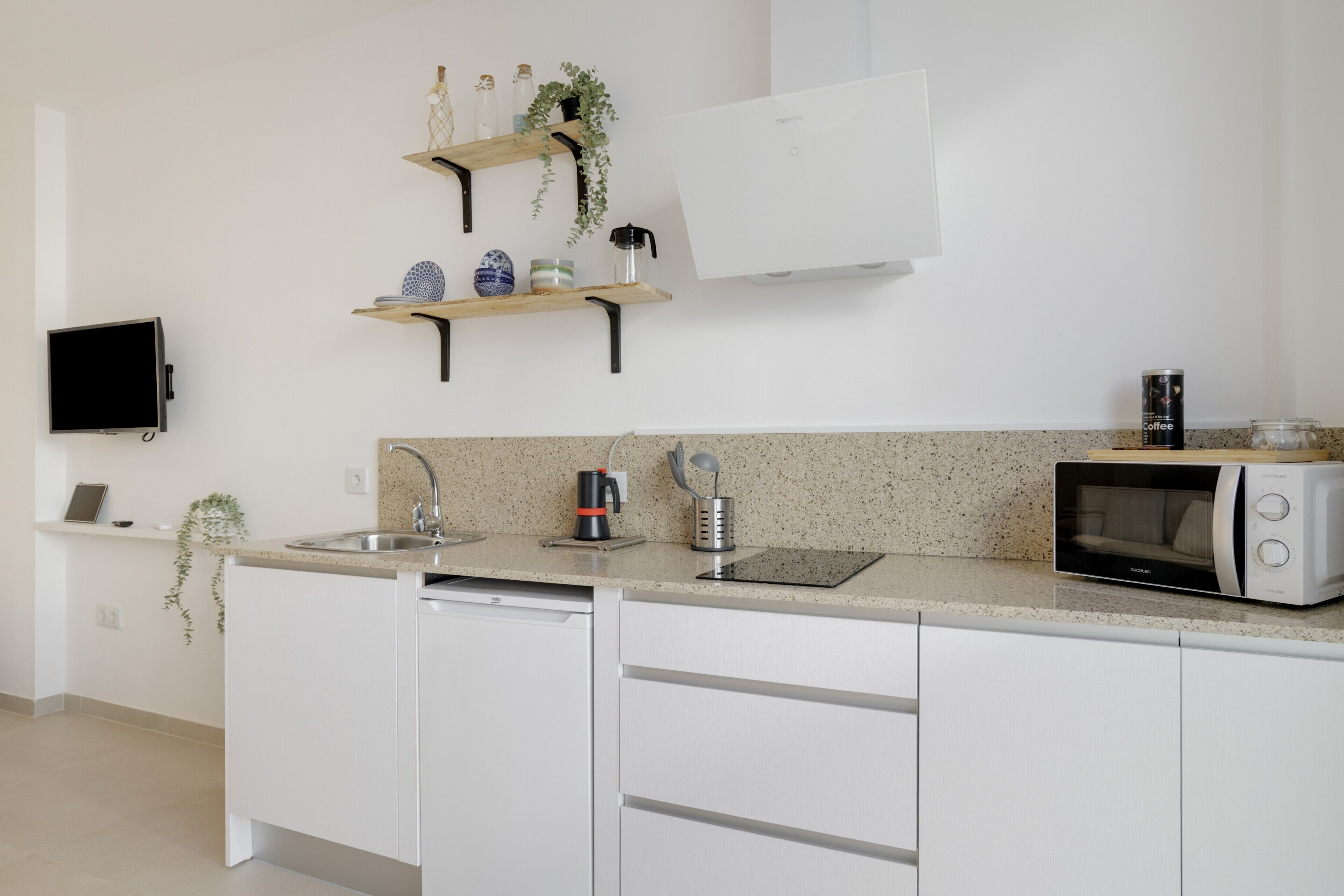 A modern kitchen with white cabinets, a dishwasher, a microwave, a coffee maker, and a TV mounted on the wall.