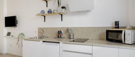 A modern kitchen with white cabinets, a dishwasher, a microwave, a coffee maker, and a TV mounted on the wall.