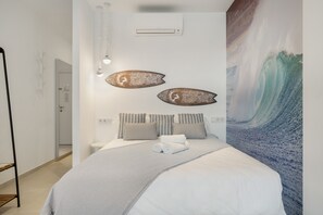 A bedroom with a bed, pillows, a wall-mounted air conditioner, and a large wave painting.