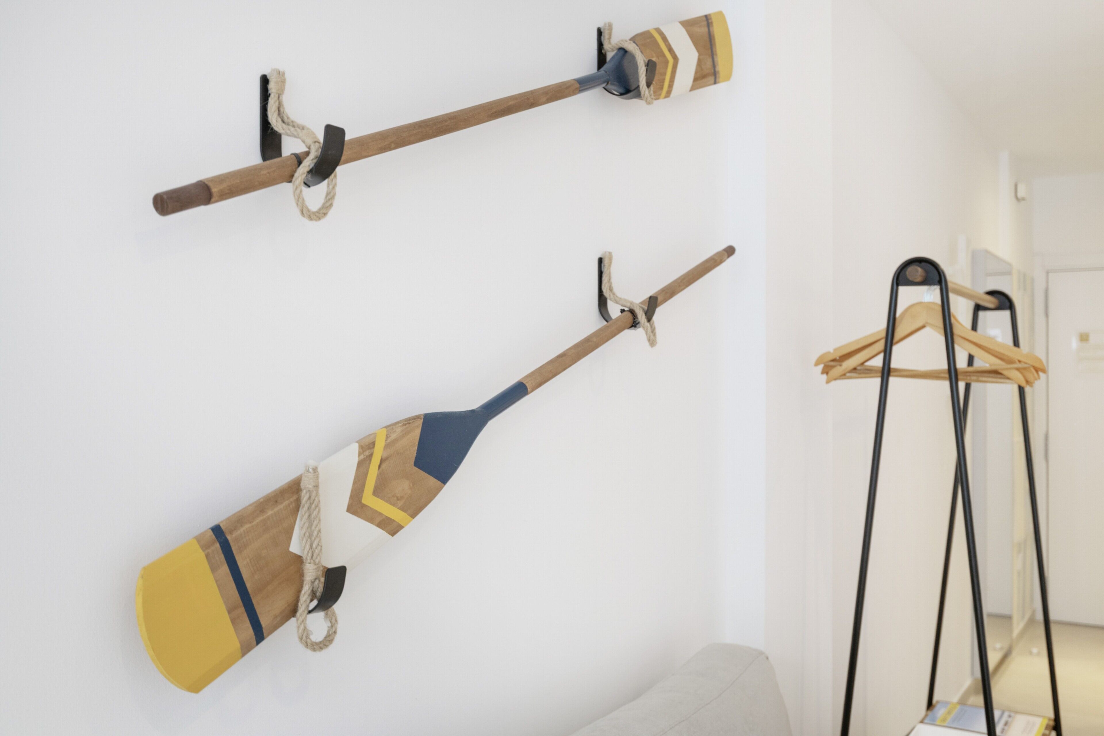 Two wall-mounted paddles, a light-colored sofa, and a black hanger stand in a room.