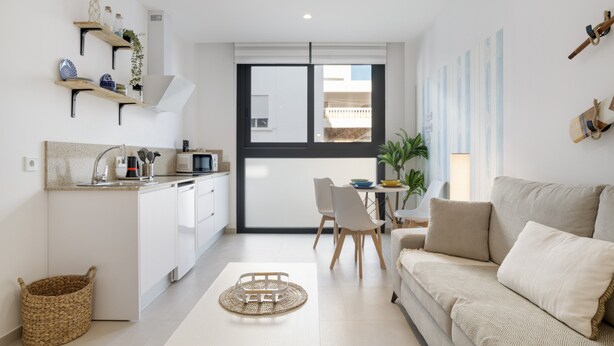 Una cocina moderna con armarios blancos, un comedor con mesa y sillas, y una sala de estar con sofá.