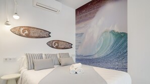 Un dormitorio con cama, almohadas, una obra de arte en la pared que representa una ola, y una mesita de noche con lámpara.