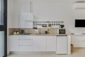 A modern kitchen with white cabinets, a microwave, a coffee maker, and a hanging pot rack.