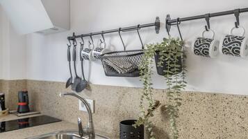 A kitchen with a stainless steel sink, a black hanging rack with utensils, and a potted plant.