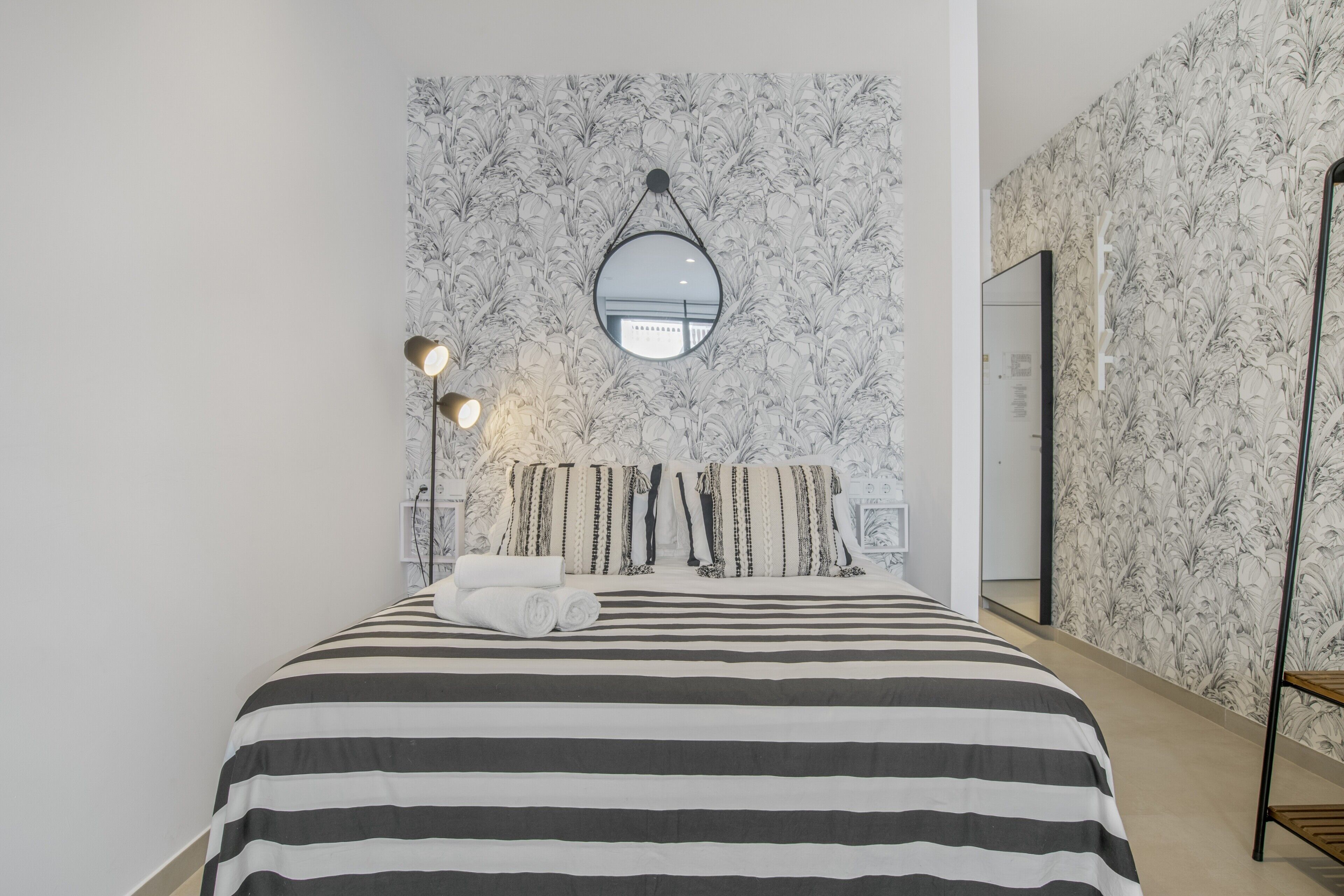 Ein Schlafzimmer mit einem gestreiften Bett, einem runden Spiegel und einer Stehlampe.