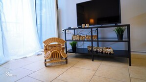 Una sala de estar con un televisor sobre un soporte negro, una silla de mimbre y un estante con adornos.