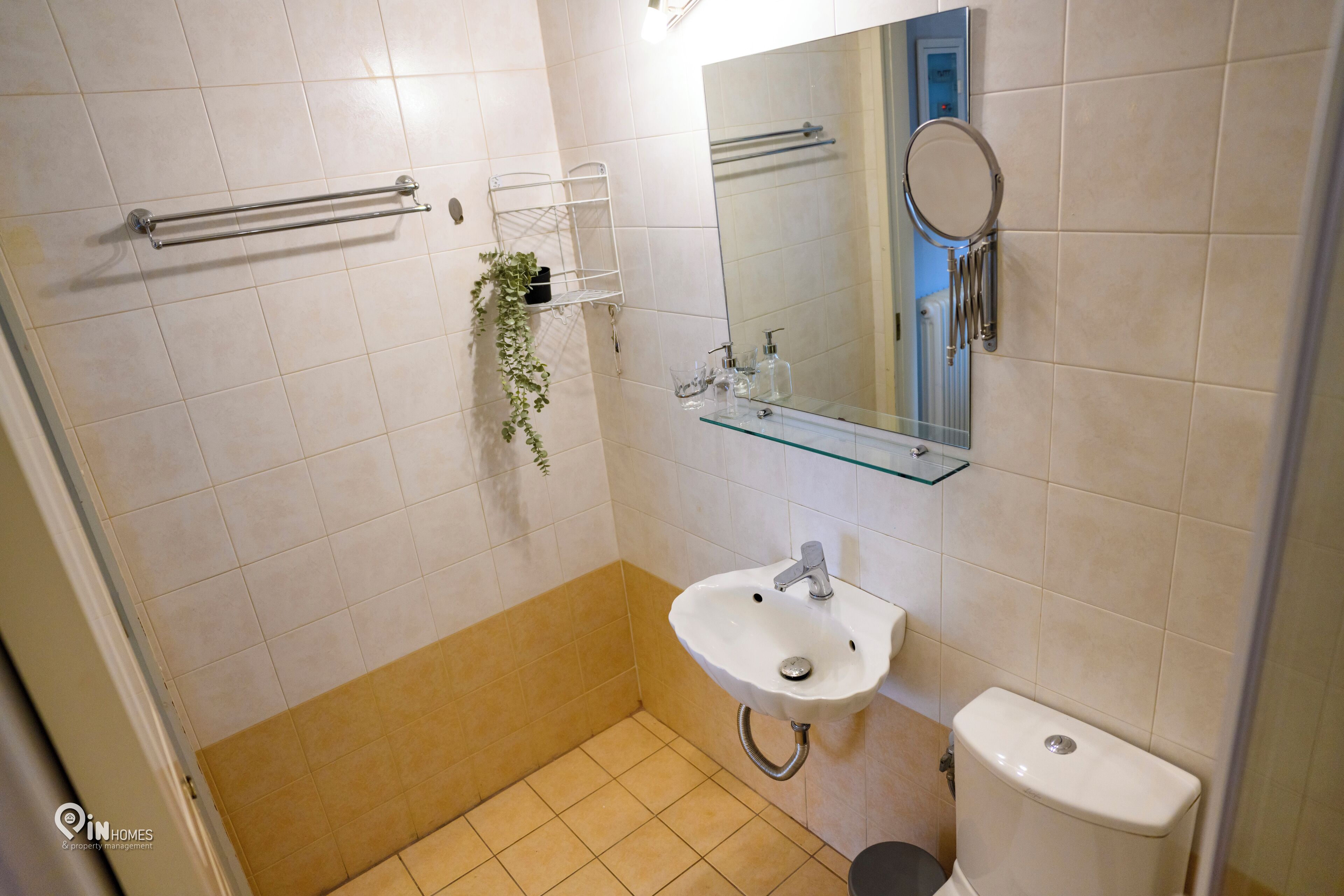Un baño con lavamanos, inodoro y repisa de vidrio con artículos de aseo.