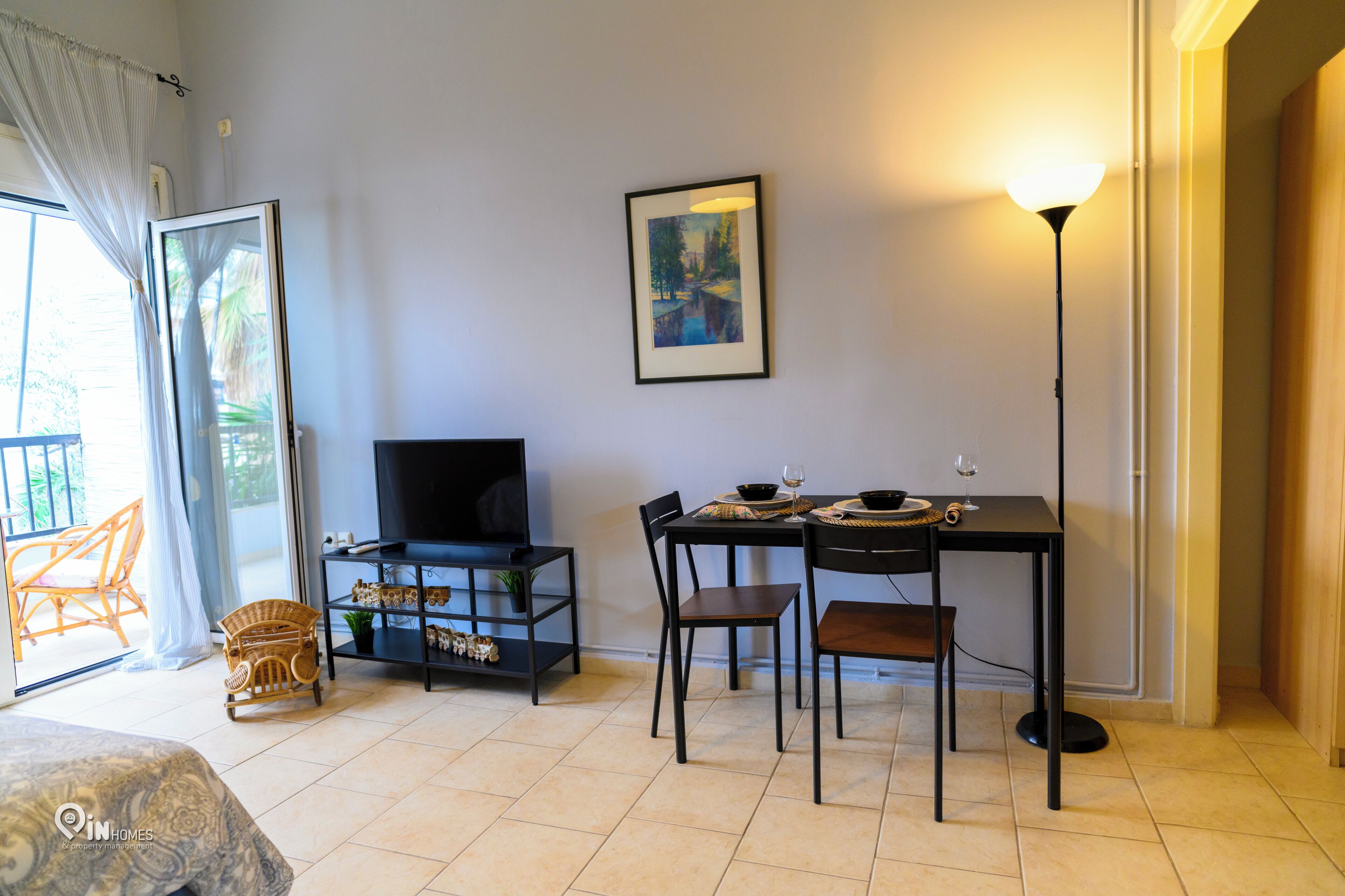 Una habitación con cama, televisor, mesa de comedor con sillas, un cuadro en la pared y una lámpara.