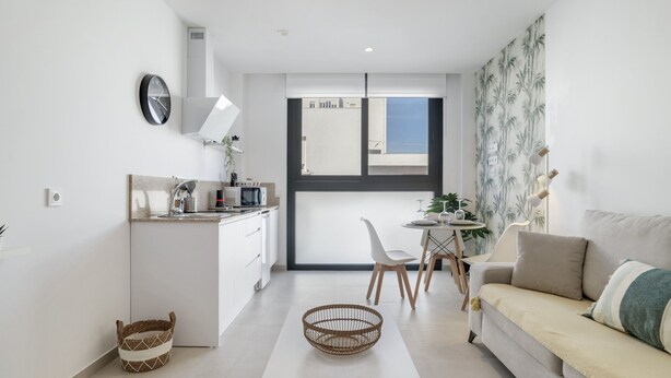 Een moderne keuken met witte kasten, een eetgedeelte met een witte tafel en stoelen, en een woongedeelte met een bank en een plant.