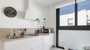 Een moderne keuken met een spoelbak, magnetron en een klok aan de muur.