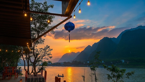 Ein Sonnenuntergangsblick von einer Terrasse mit Holzmöbeln und Lichterkette.