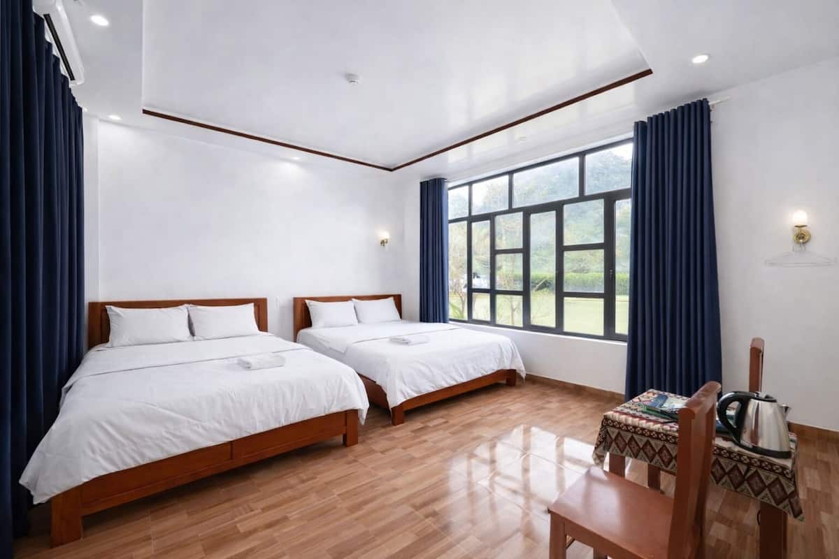 Une chambre d’hôtel avec deux lits en bois, une table en bois avec une bouilloire et une grande fenêtre avec des rideaux.