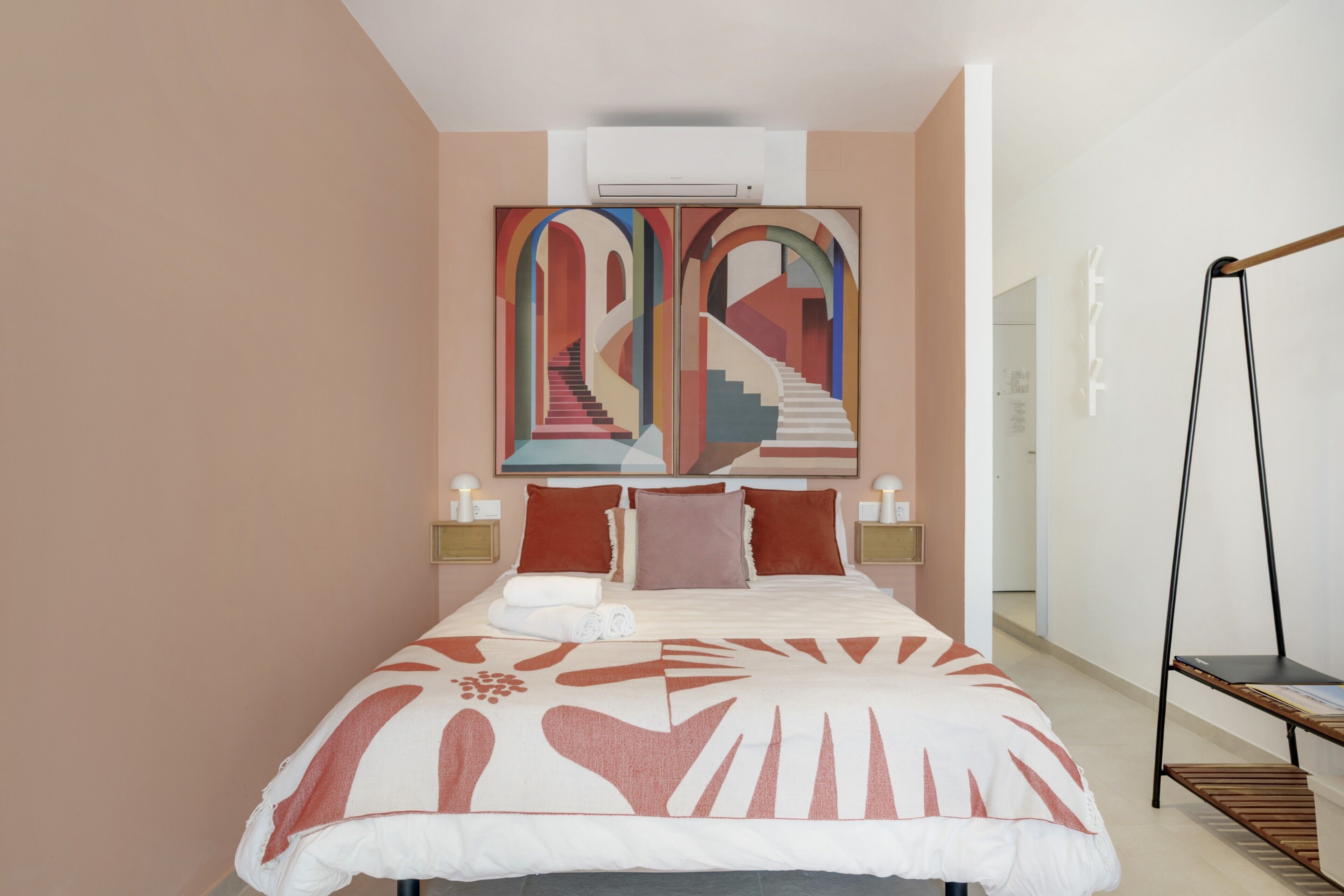 Une chambre moderne avec un grand lit, un climatiseur fixé au mur, une table de chevet avec une lampe et un fauteuil suspendu.