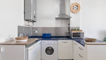 A compact kitchen with a washing machine, microwave, and a clock on the wall.