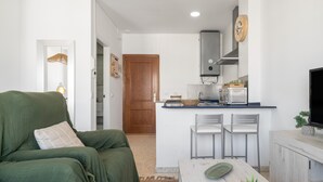 A compact living space with a sofa, a dining table, a kitchen area with a microwave, and a television. - 'San Mateo Loft' Studio with Communal Pool, Wi-Fi, and Air Conditioning (Tarifa)
