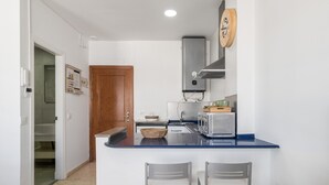 A compact kitchen with a built-in stove, a microwave, and a toaster. There are two bar stools and a wooden door leading to a hallway. - 'San Mateo Loft' Studio with Communal Pool, Wi-Fi, and Air Conditioning (Tarifa)