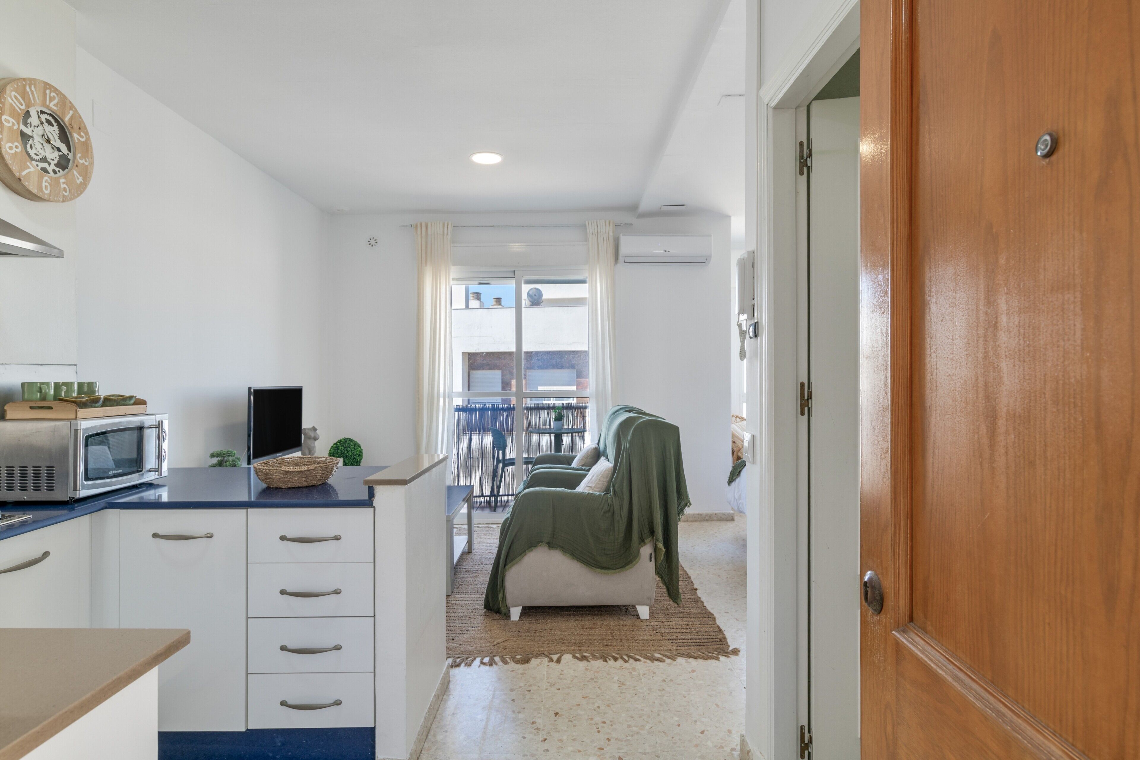 A compact living space with a kitchenette, a sofa, and a view to an outdoor balcony.