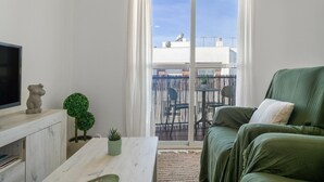 A living room with a sofa, a television, a small table, a potted plant, and a sliding glass door leading to an outdoor balcony. - 'San Mateo Loft' Studio with Communal Pool, Wi-Fi, and Air Conditioning (Tarifa)
