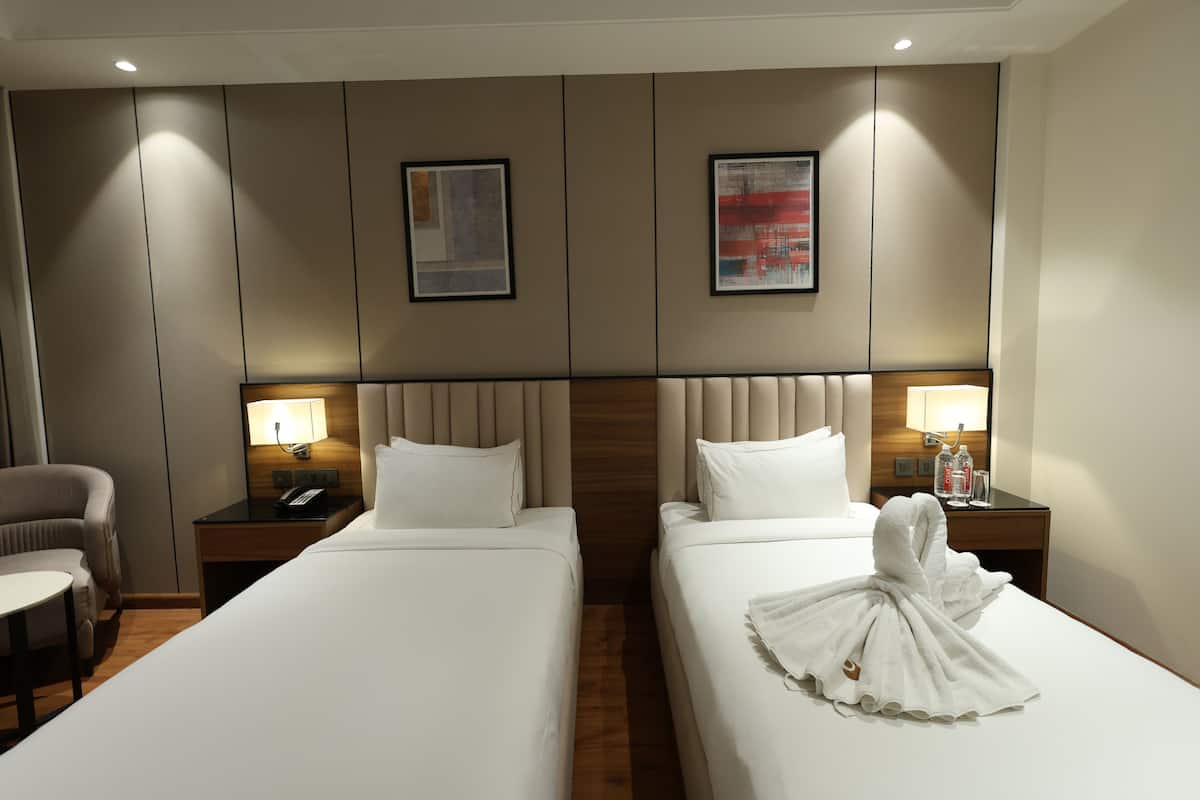 Une chambre d’hôtel avec deux lits, une chaise, un bureau et une table de chevet avec une lampe.