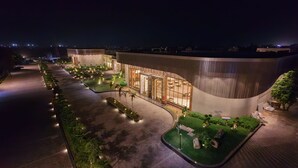 Um hotel moderno com fachada curva, jardins ajardinados e entrada bem iluminada.