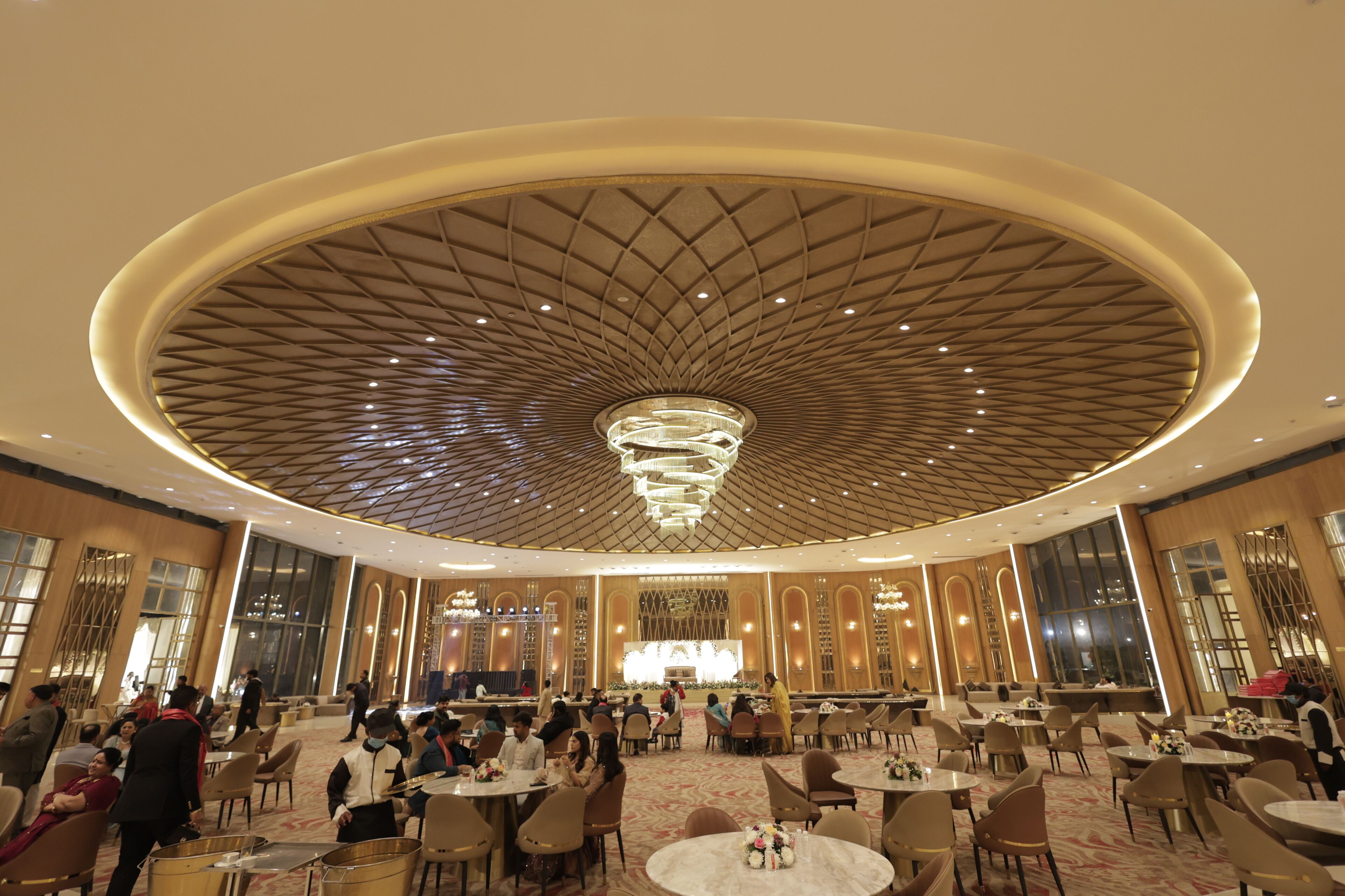 A spacious hotel lobby with a large circular ceiling design, multiple seating areas, and a stage in the background.