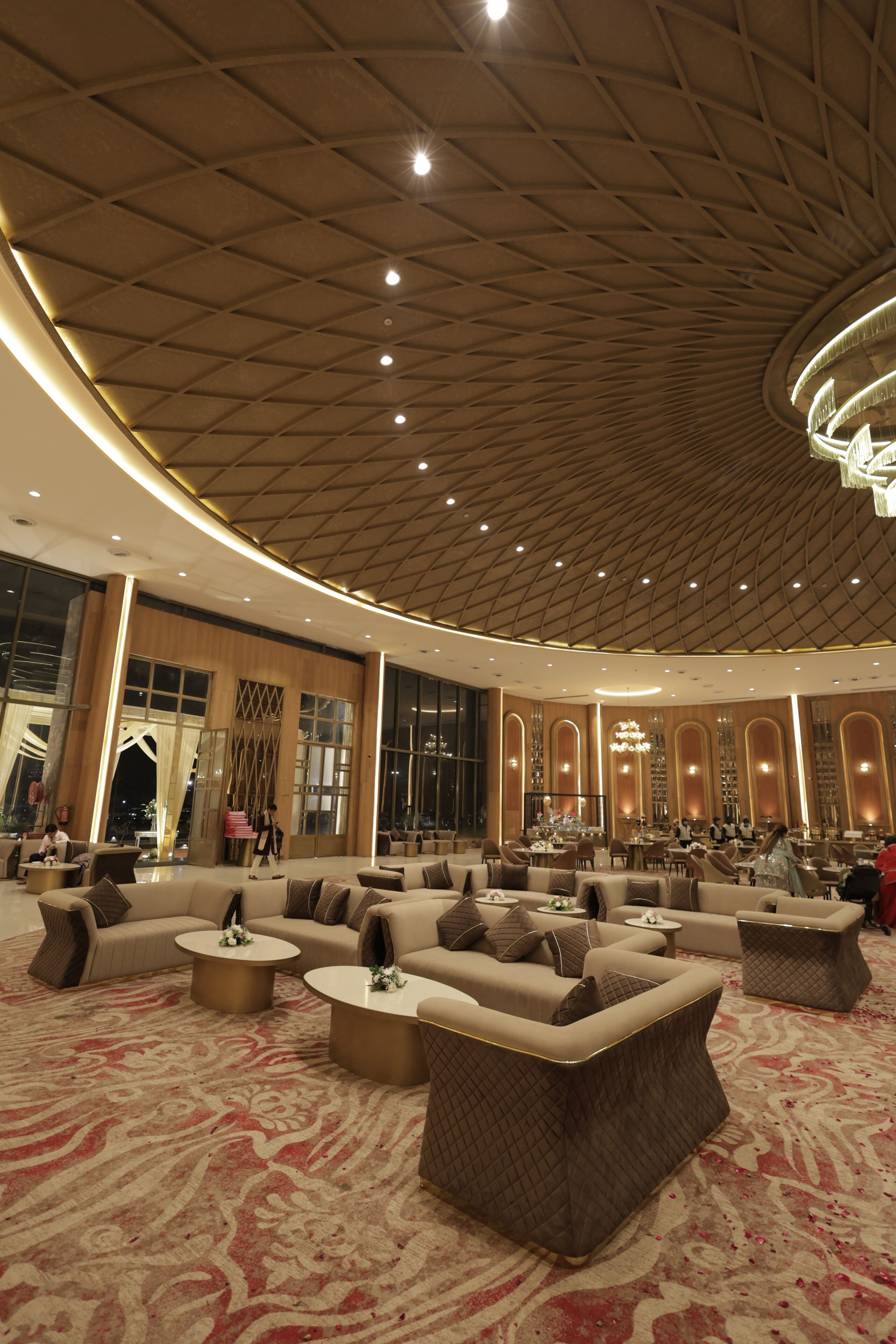 A spacious lobby with a high ceiling, large windows, and a central seating area with sofas and round tables.