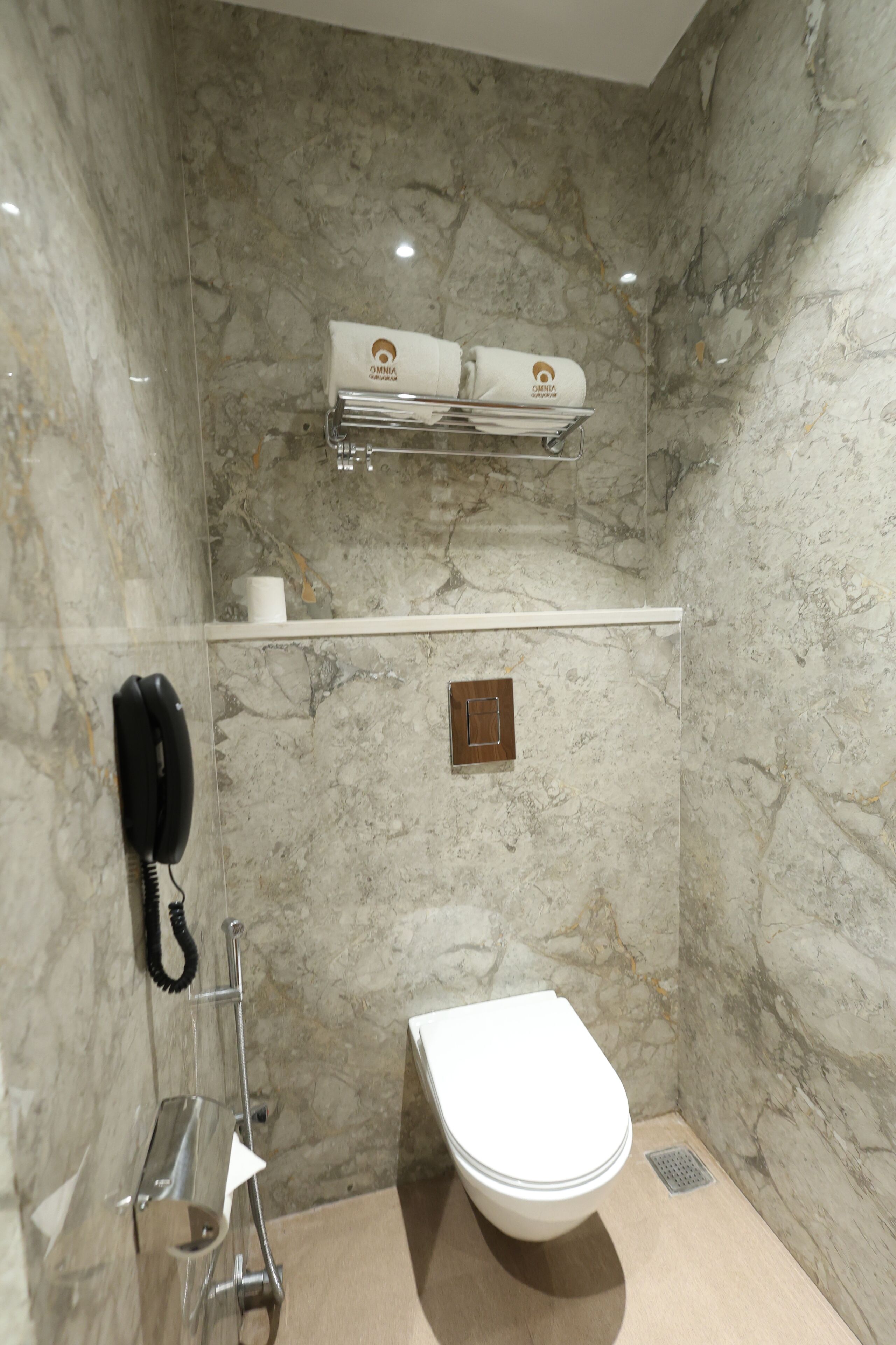 Un baño con pared de mármol, inodoro, secamanos y teléfono.