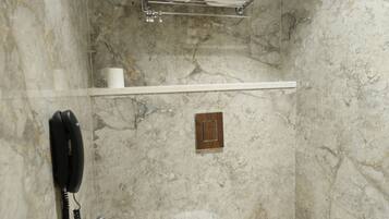 Un baño con pared de mármol, inodoro, secamanos y teléfono.