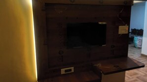 A dark wooden TV stand with a flat-screen TV, a power outlet, and a small ventilation slot. - Panchmukhi Home Stay  (Varanasi)