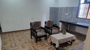 A room with a herringbone floor pattern, two patterned armchairs, a small table with a vase, and a window with a metal grill. - Panchmukhi Home Stay  (Varanasi)