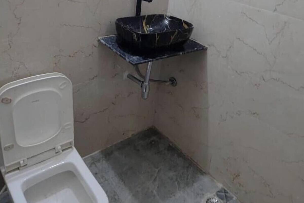 A small bathroom with a toilet, a black sink on a metal stand, and a shelf above the sink.