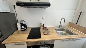 A compact kitchen with a black induction cooktop, a stainless steel sink, and a built-in oven. - Les roses" studio: cosy and comfortable (Mulhouse)