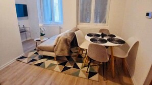 Un espace de vie compact comprenant un canapé, une table à manger avec des chaises, un petit coin cuisine et une fenêtre avec des rideaux.