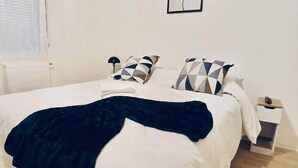 Une chambre à coucher avec un lit, des oreillers, une couverture, une table de chevet, une lampe et un tableau accroché au mur.