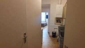 A narrow hallway leading to a bedroom with a bed and a small window. A kitchen area is visible with a sink and cabinets. - Group Stay 3 Apts Near Enkplatz (Vienna)