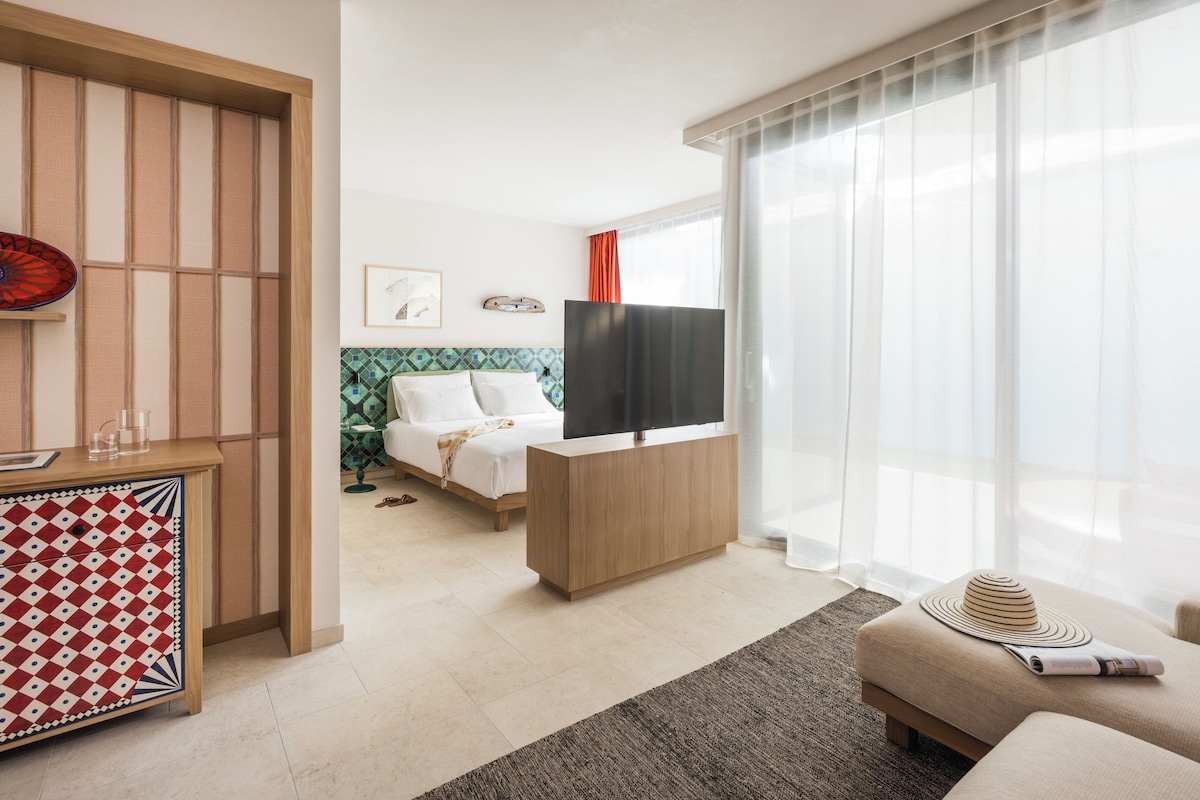 A modern hotel room with a bed, a TV, a desk, and a sofa.