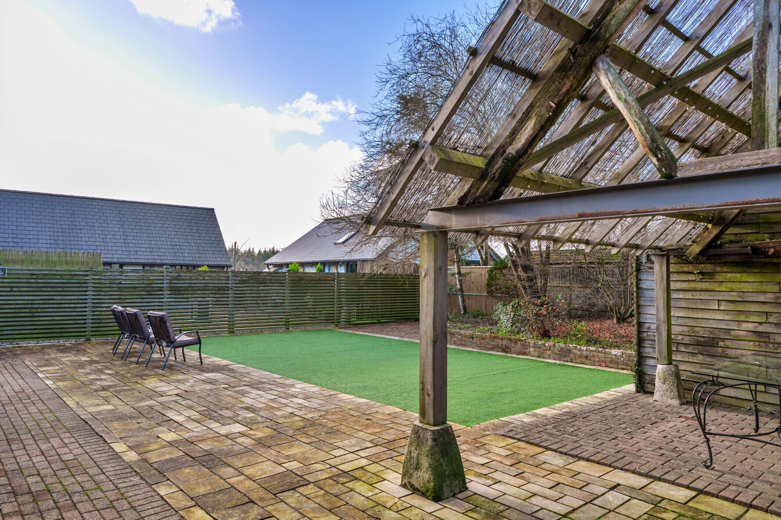 A covered patio area with a brick floor, a green artificial turf, and a wooden pergola structure.