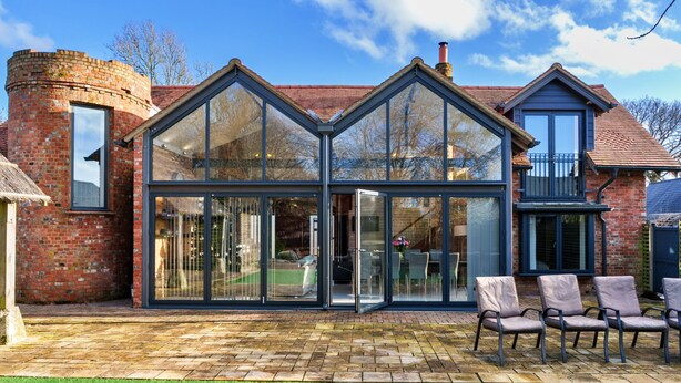 Een modern huis met een glazen conservatorium, een bakstenen schoorsteen en een keurig onderhouden tuin.