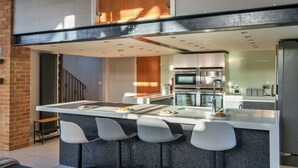 Een moderne keuken met een centraal eiland, barkrukken, roestvrijstalen apparatuur en een bakstenen muur.