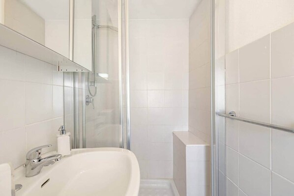 Une salle de bain avec une baignoire blanche, une douche en verre et un mur recouvert de carreaux blancs.