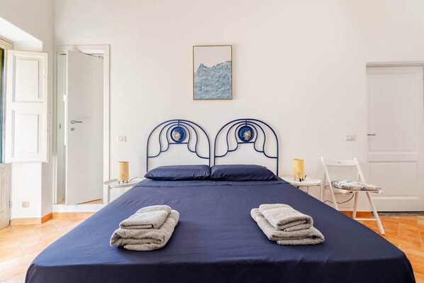 A bed with a metal frame, two pillows, a blue bedspread, and two folded towels. - Pietra Longa - Apartment with sea-view terrace (Lipari)
