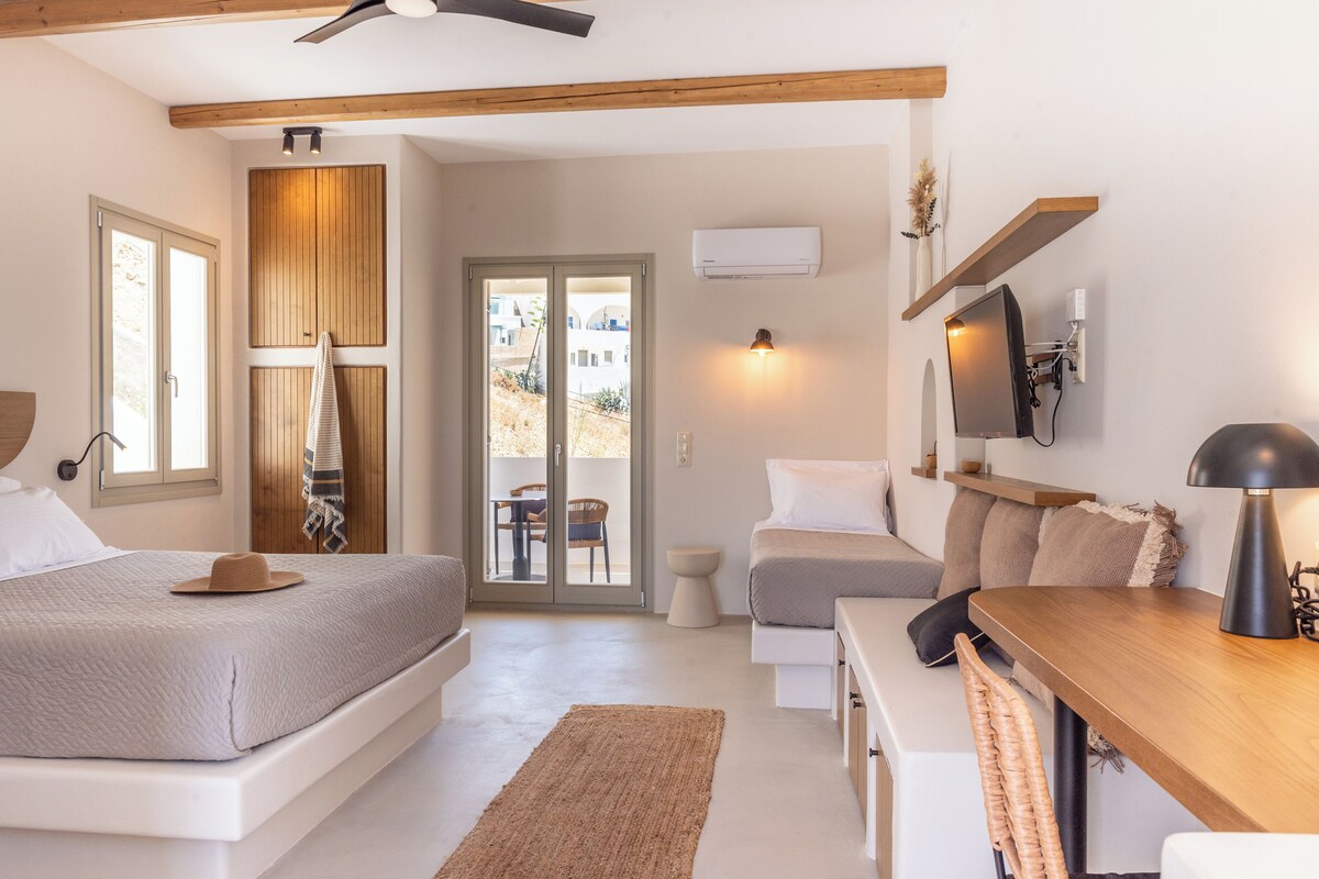 Ein Schlafzimmer mit einem Bett, einem Nachttisch und einem Schreibtisch mit Stuhl. Es gibt ein Fenster, eine Tür und einen Deckenventilator.