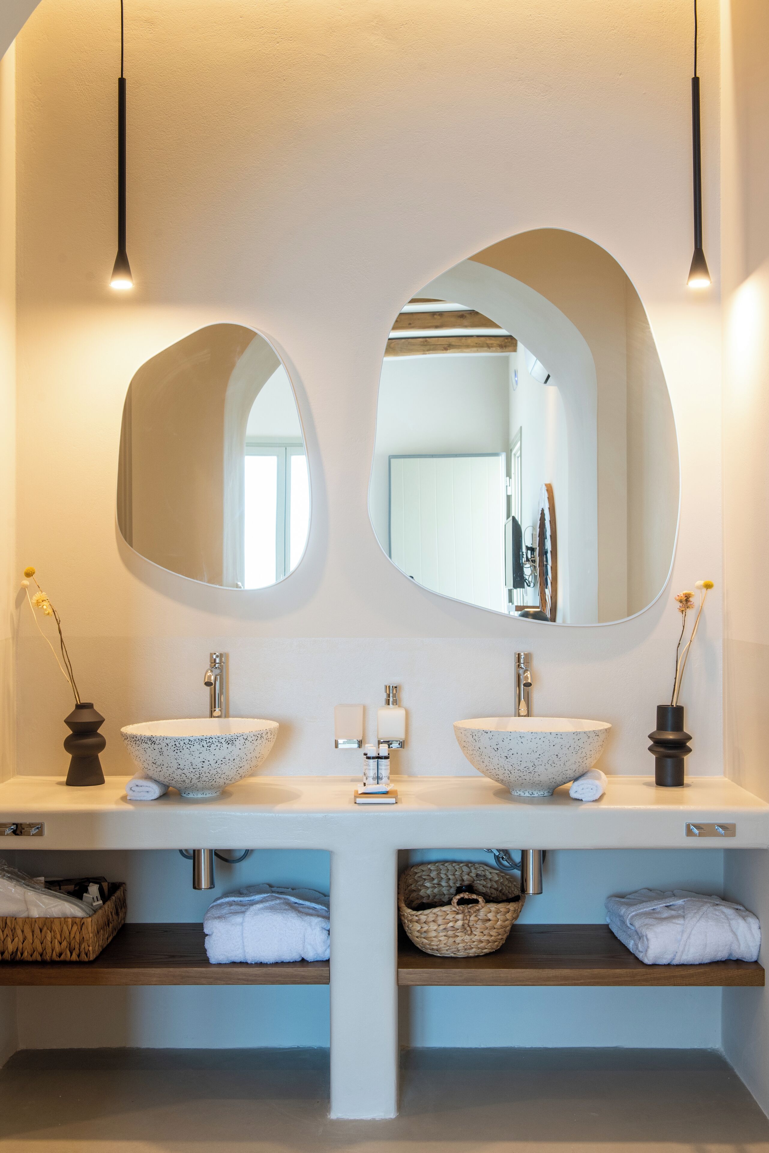 Une salle de bain moderne avec deux grands miroirs ronds, un lavabo blanc à motifs et une étagère en bois en dessous.