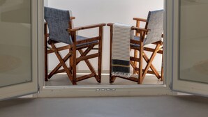 Een kamer met uitzicht op zee, twee houten stoelen en een glazen deur.