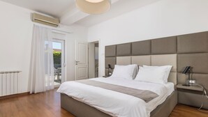 Une chambre moderne avec un grand lit, une tête de lit, une table de chevet avec une lampe, et une vue sur l’extérieur grâce à une porte coulissante.