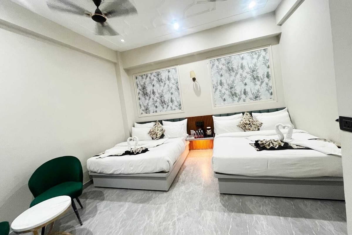 A hotel room with two beds, a green chair, a small table, and a ceiling fan.