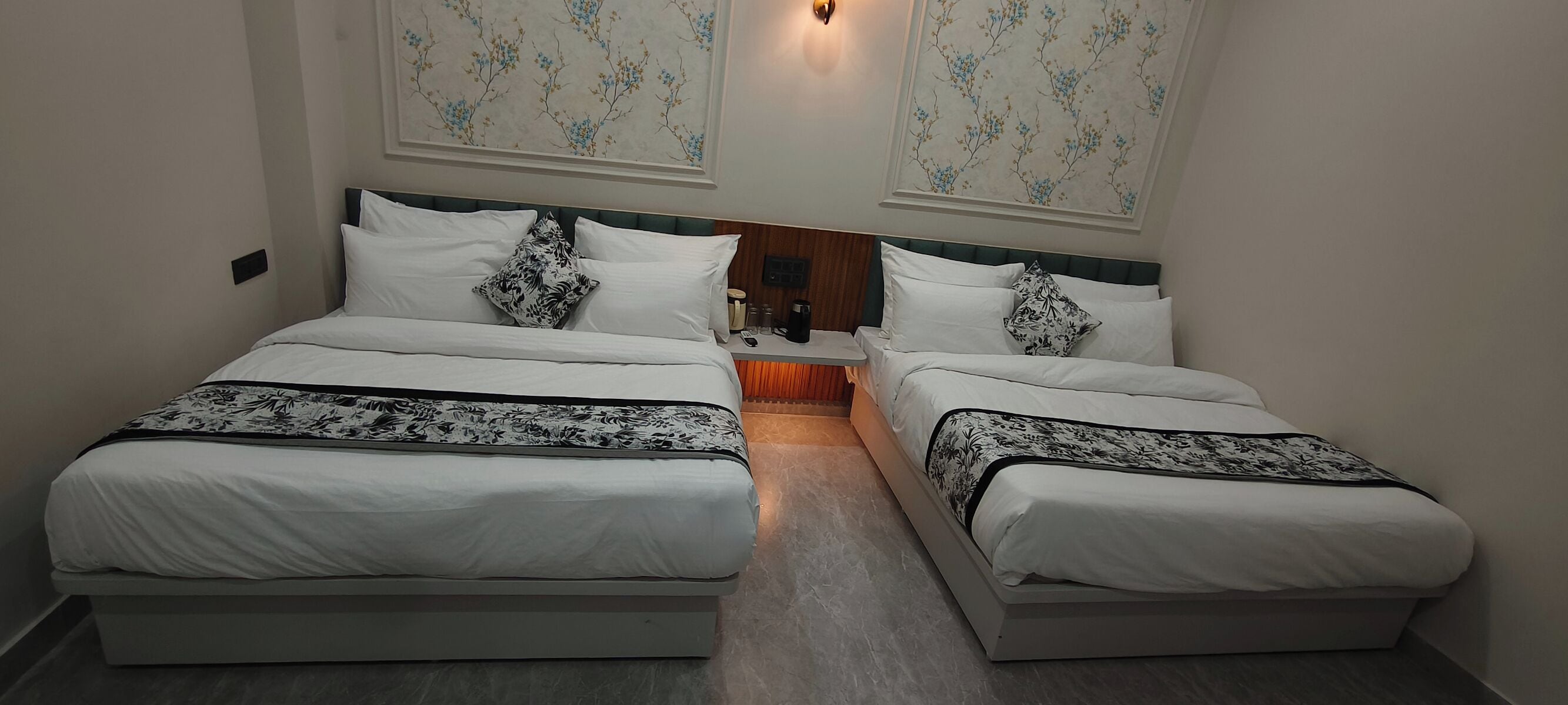 Een hotelkamer met twee bedden, elk met een beddeken met dessin en passende kussens. Er staat een klein tafeltje met een lamp en een decoratieve wandversiering boven de bedden.
