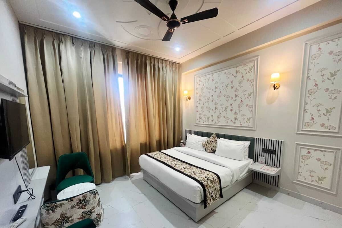 A hotel room with a bed, a desk with a chair, a television, and a ceiling fan.