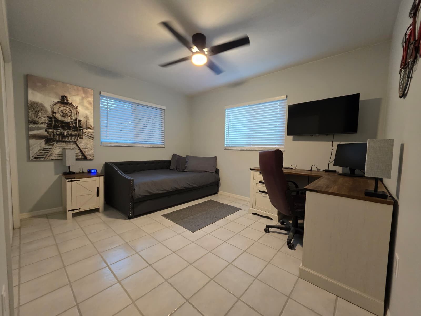 A compact living space with a sofa, a desk, a chair, a TV, and a ceiling fan.
